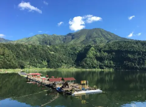 Telaga di kawasan Dieng dengan rakit apung dan bukit hijau